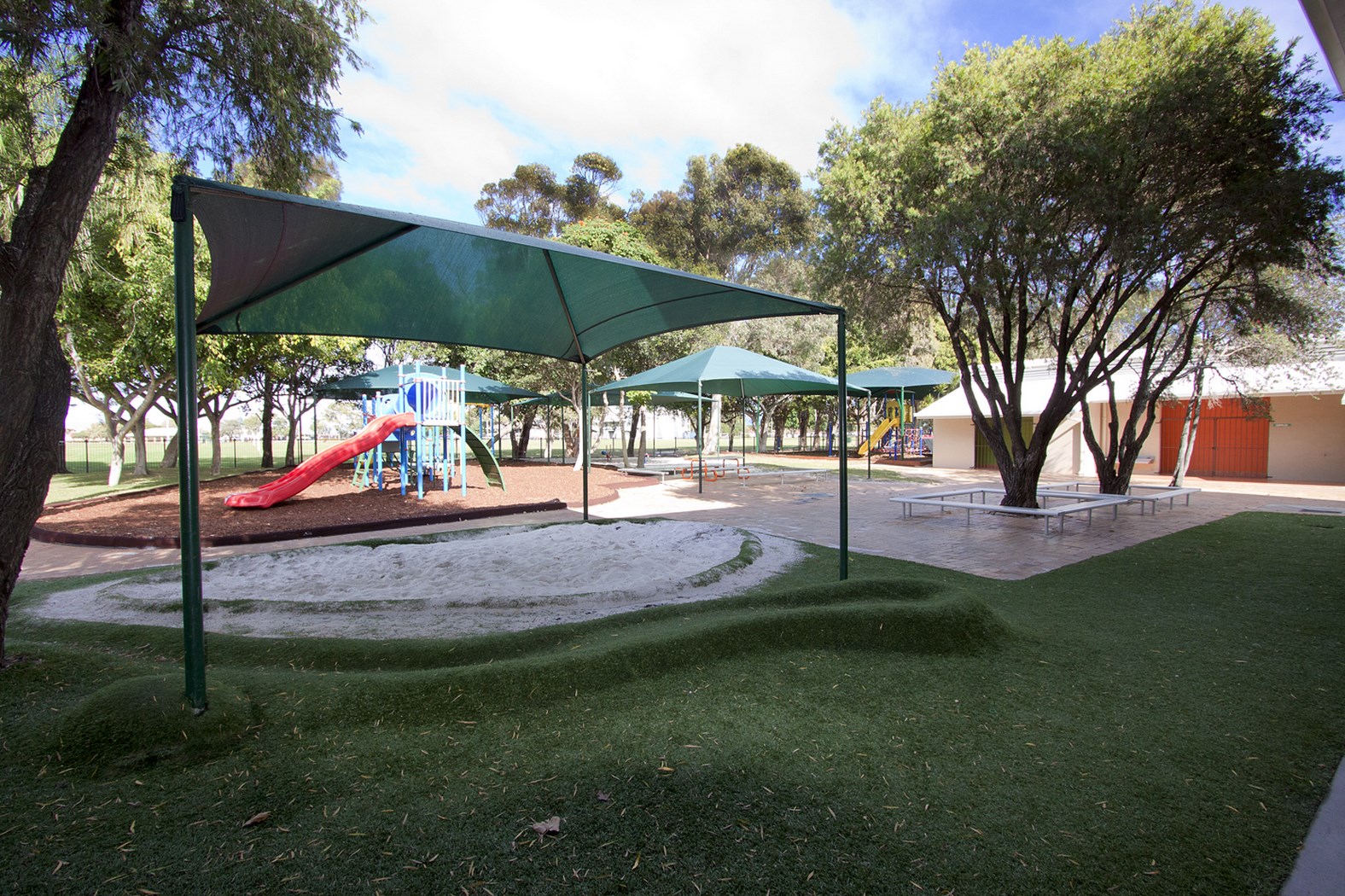 Primary school playground with shaded seating, sandpit and play equipment, supporting safe outdoor play, social interaction and active learning