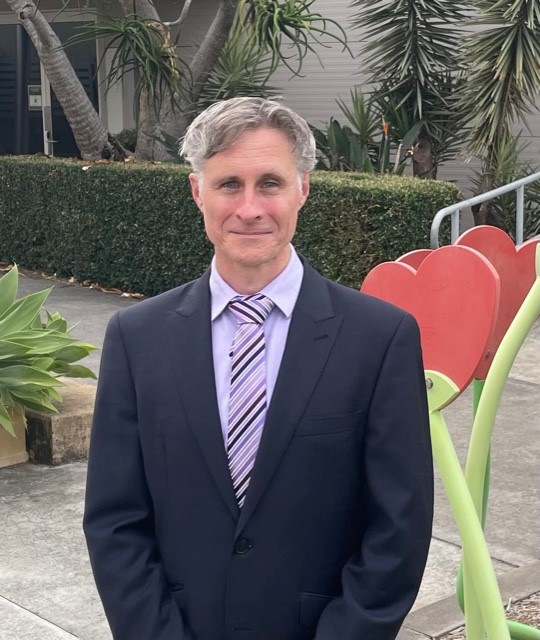 Staff member in formal attire standing outdoors on school grounds highlighting leadership presence and connection to the school community